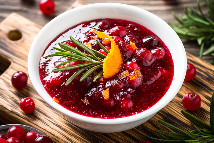 A bowl of cranberry sauce on top a wooden chopping board.