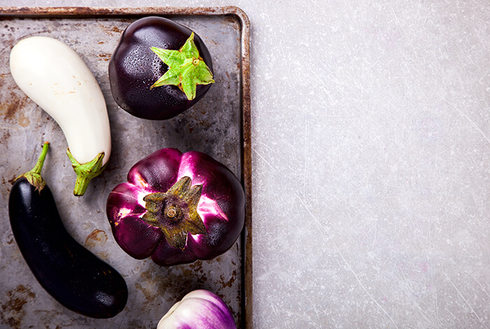 Different types of raw eggplants on a tin tray. 