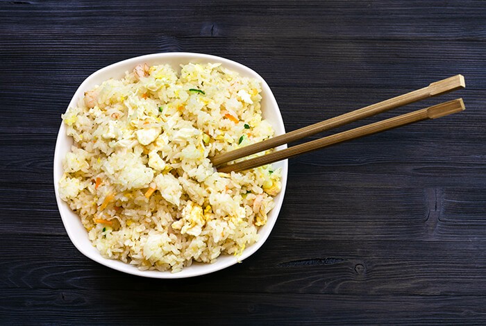 Yang chow fried riced placed in a white bowl with wooden chopsticks.