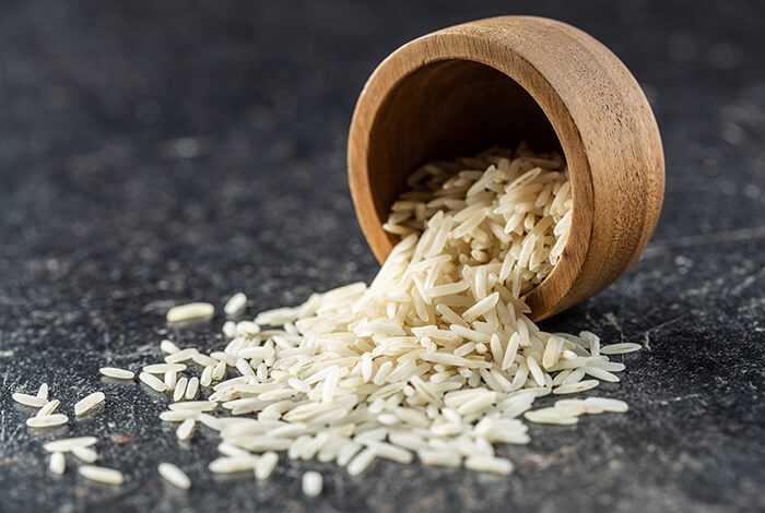 Uncooked jasmine rice spilled from a small wooden bowl.