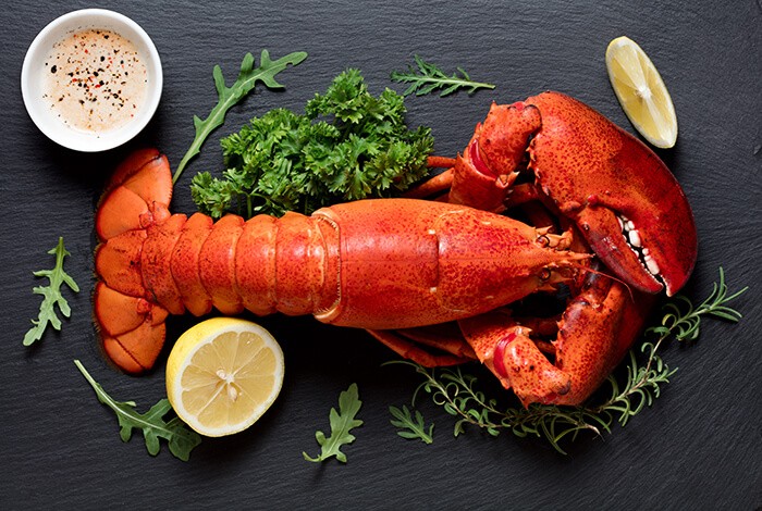 Cooked lobster with lemon, herbs, and dip and placed on a black surface. 