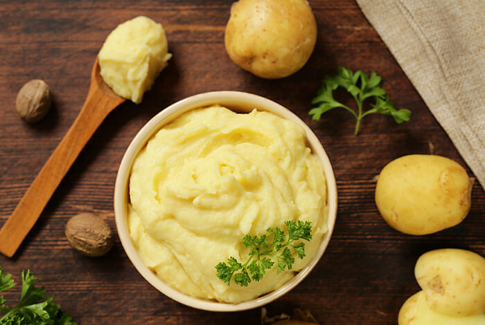 A bowl of mashed potatoes surrounded by raw potatoes.