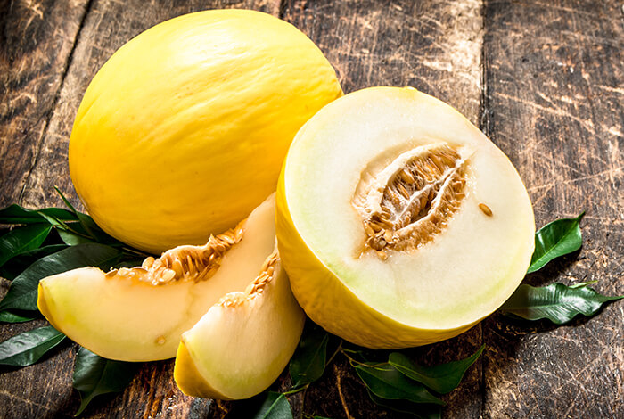 Slices of honeydew melon and a whole honeydew melon.
