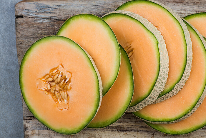Slices of cantaloupe spread out on a wooden board.