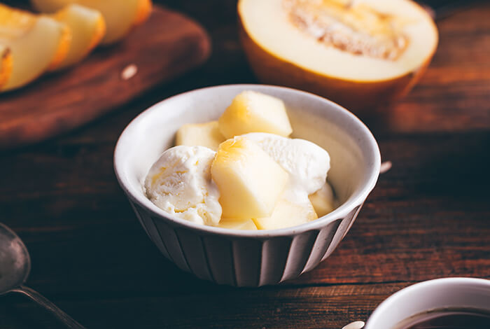 A bowl of vanilla ice cream topped with pieces of melon.