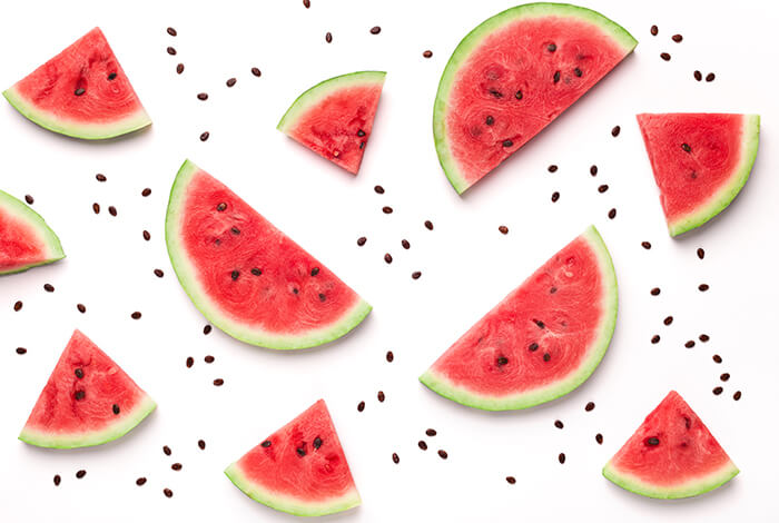 Slices of watermelon and seeds scattered on a white surface.