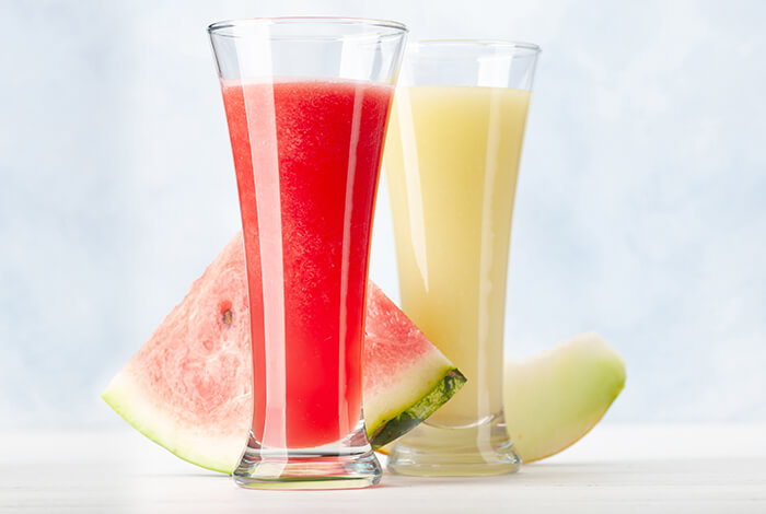 Two glasses of watermelon and melon shakes and their fruit slices.