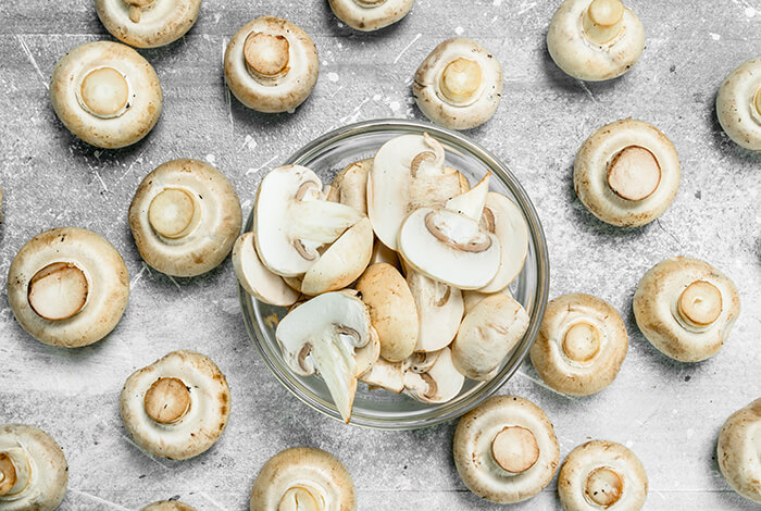 A bowl of sliced mushrooms surrounded by button mushrooms.