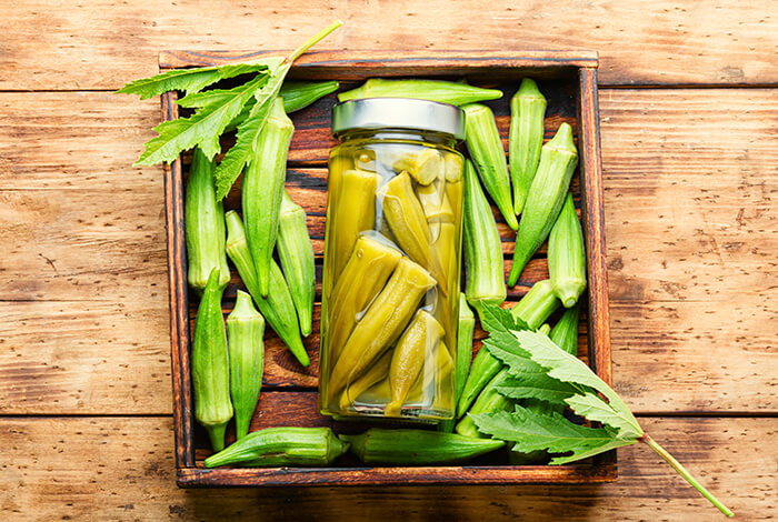 A jar of pickled okra placed beside fresh okra.