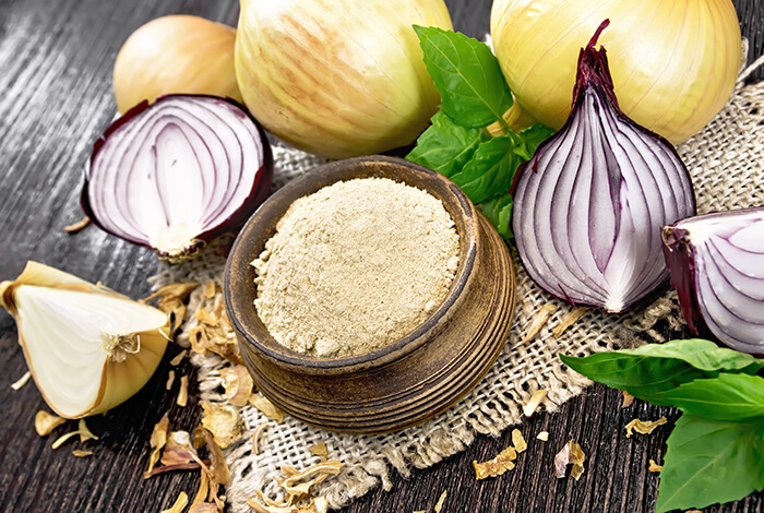 A small bowl filled with onion powder and surrounded by different types of onions.