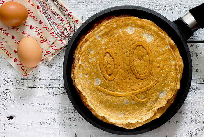 Pancakes on a pan with eggs on the side.