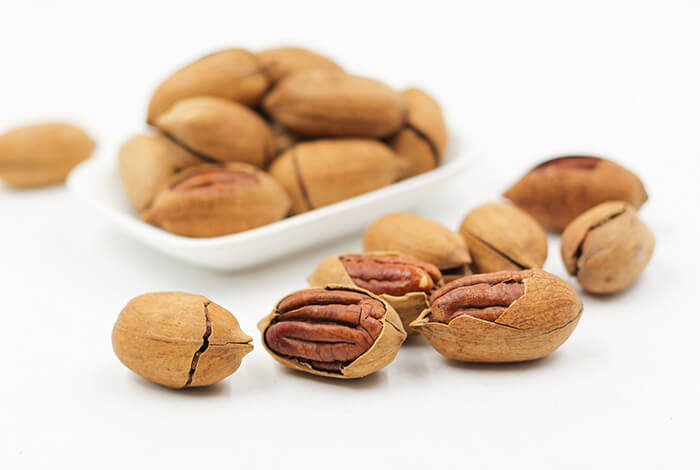 Cracked pecans in the foreground and a plate of cracked pecans in the background.
