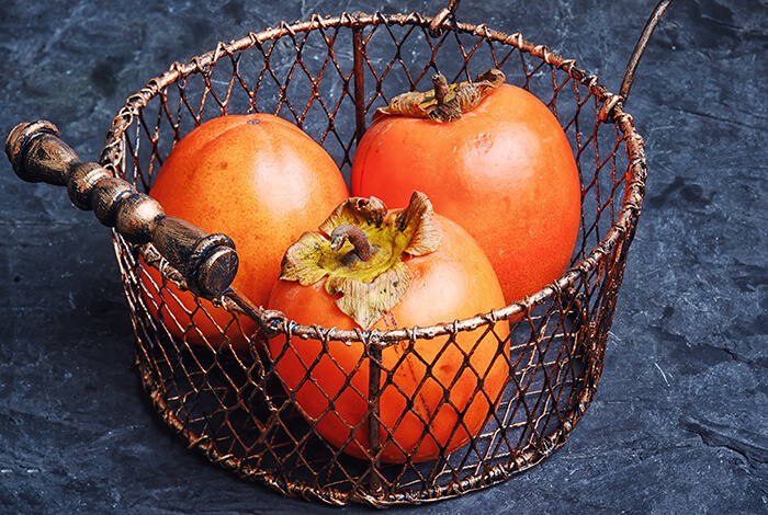 A metal basket filled with persimmons.