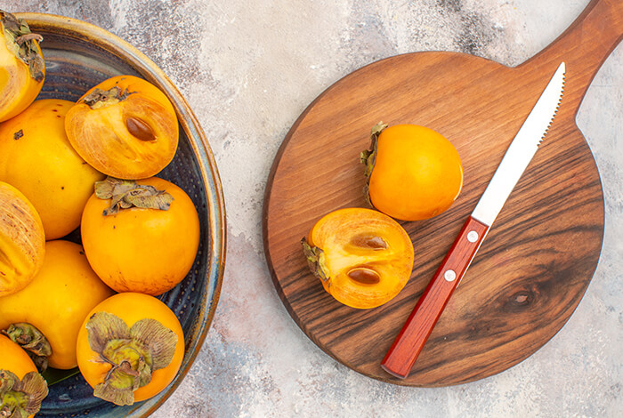 A persimmon sliced in half and a basket filled with ripe persimmons.