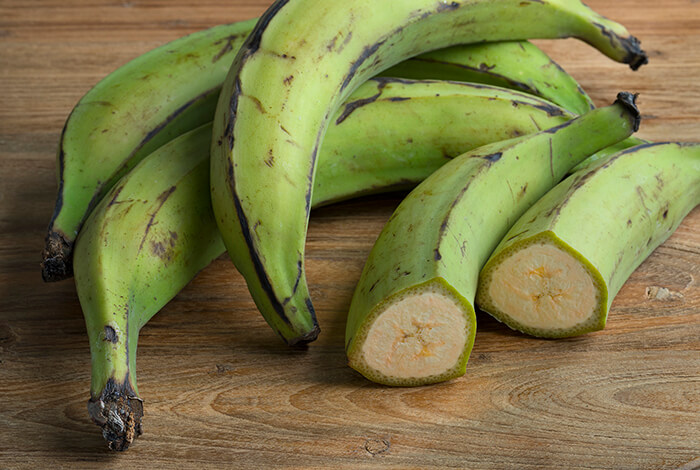 Pieces of green plantains on a wooden surface.
