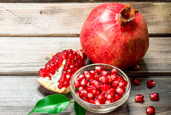 A bowl full of pomegranate seeds and a pomegranate fruit.