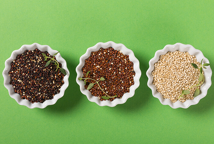 Three different types of quinoa on small white bowls.