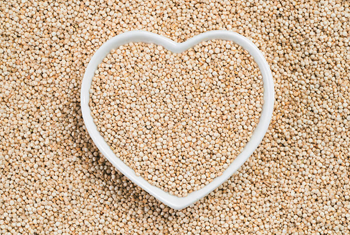 Raw quinoa filling up a heart-shaped bowl.