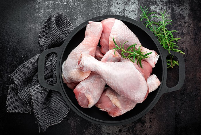 Raw chicken drumsticks filling an iron pot.