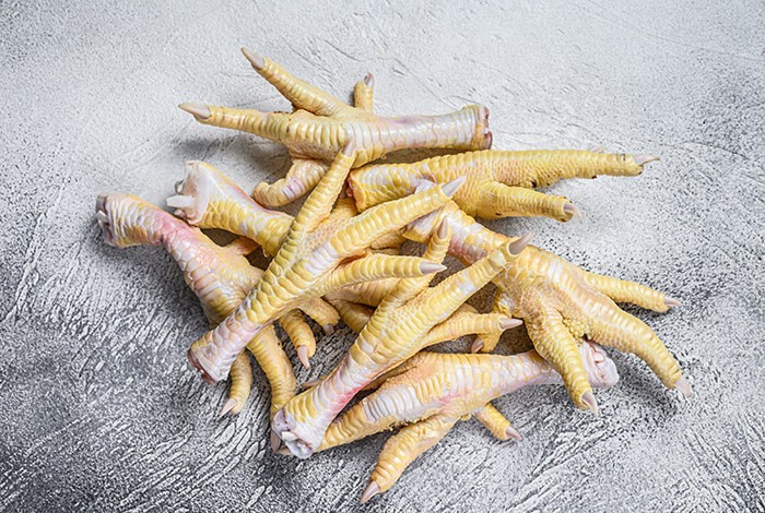 Raw chicken feet piled up on a cement surface.