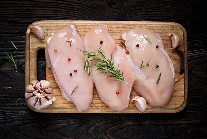 Three pieces of seasoned raw chicken fillet on top of a wooden chopping board.