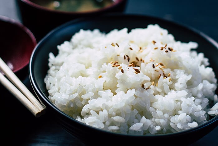 A bowl of cooked white rice sprinkled with toasted sesame seeds.