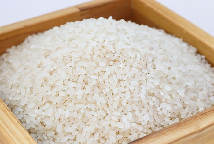 Uncooked white rice placed in a wooden square bowl.