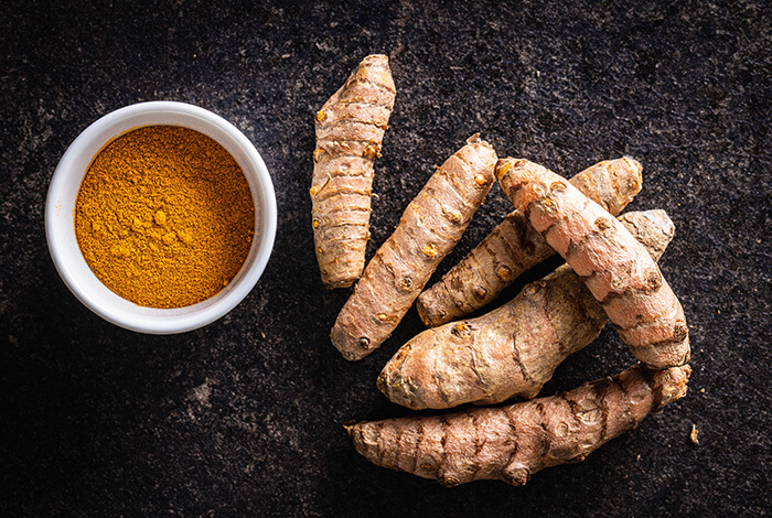 A bowl filled with turmeric powder with turmeric roots on the side. 