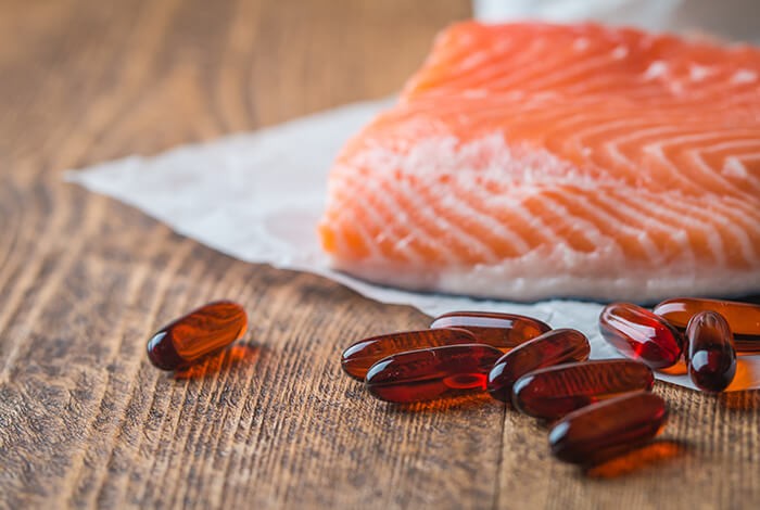 A few pieces of salmon oil capsules and a filleted salmon in the background.