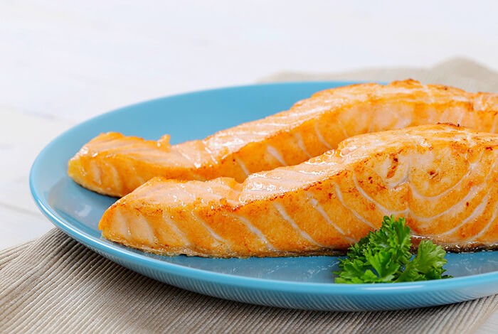 Two slices of cooked salmon placed on a blue plate.