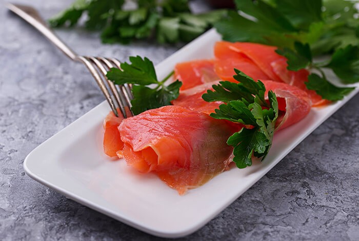 A few pieces of smoked salmon placed on a white, rectangular serving plate.