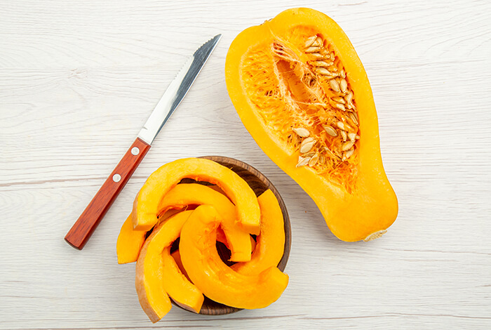 A squash sliced in half and slices of squash in a wooden bowl.