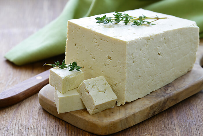 A block of herbed tofu on a wooden chopping board. 