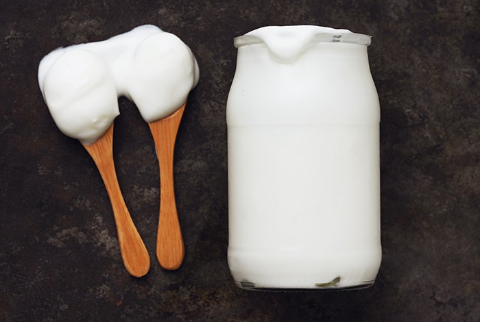 A jar filled with plain yogurt and two wooden spoons with yogurt.