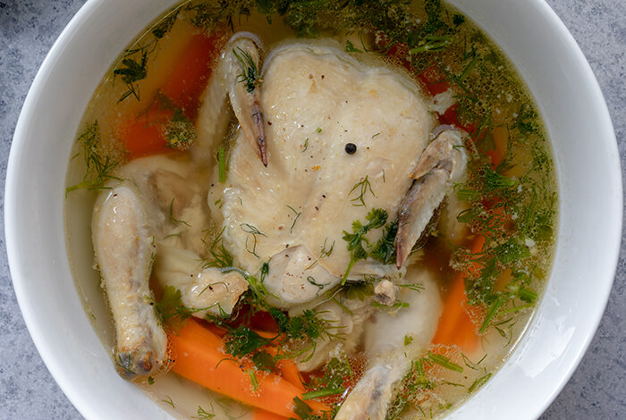 A bowl of broth with whole chicken and vegetables.