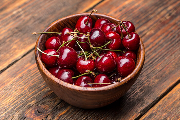 A wooden bowl filled with fresh cherries.