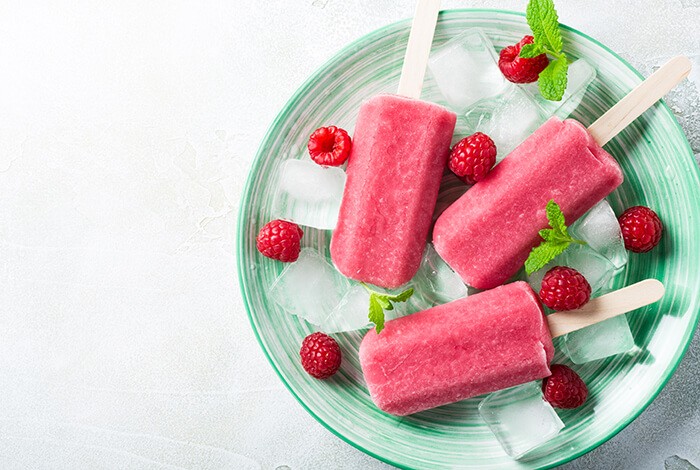 Dog raspberry ice pops with ice cubes, raspberries, and mint leaves on a plate.