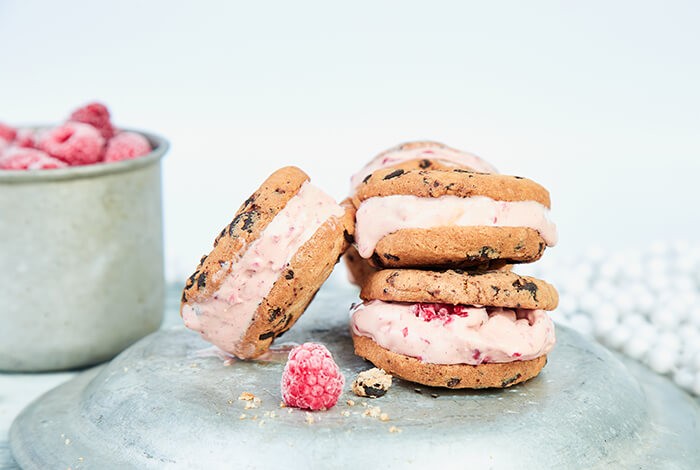 Dog berry ice cream sandwiches with a bucket of frozen raspberries in the background.