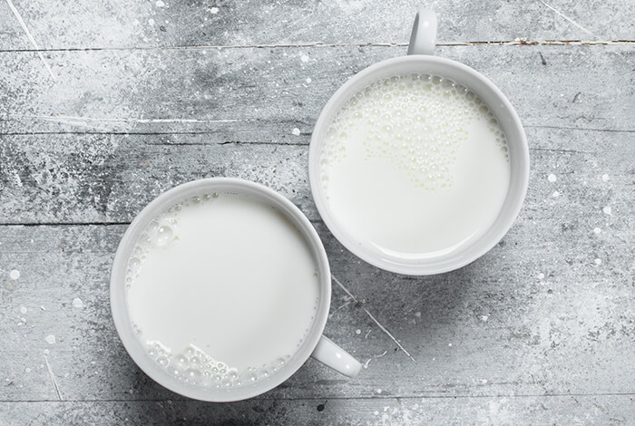 Two cups of goat's milk on a rough surface.