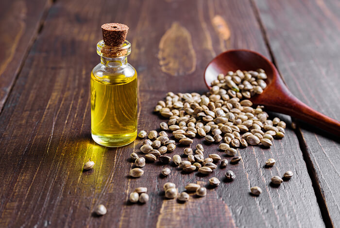 A vial of hemp oil and a spoonful of hemp seeds scattered around.