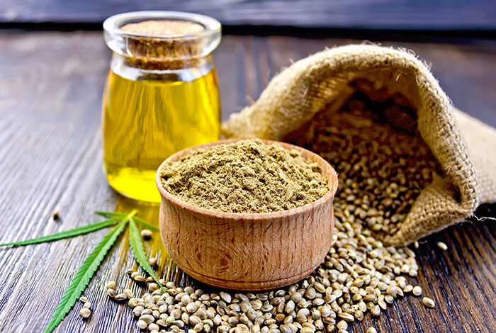 A jar of hemp oil, a bowl of hemp powder, and a burlap bag filled with hemp seeds.