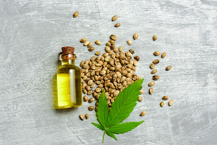 A vial of hemp oil and hemp seeds scattered around.