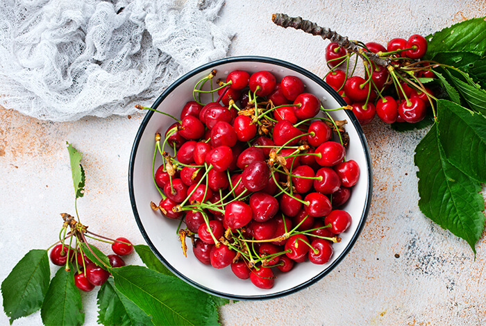 Fresh cherries in a metal bowl surrounded by two branches of cherries.