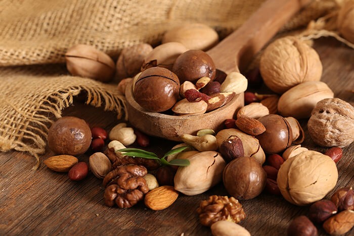 A variety of nuts, a burlap, and a wooden spoon placed on top of a wooden surface.