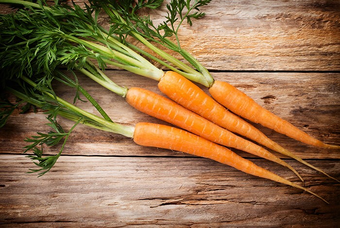 Skinny carrots with leaves placed on a wooden surface.