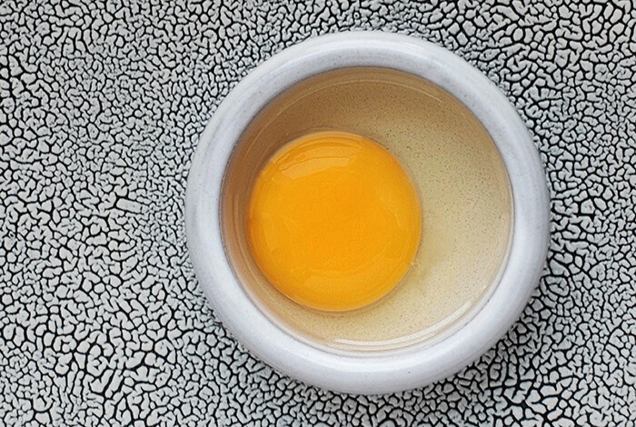 A raw egg in a white ceramic bowl.