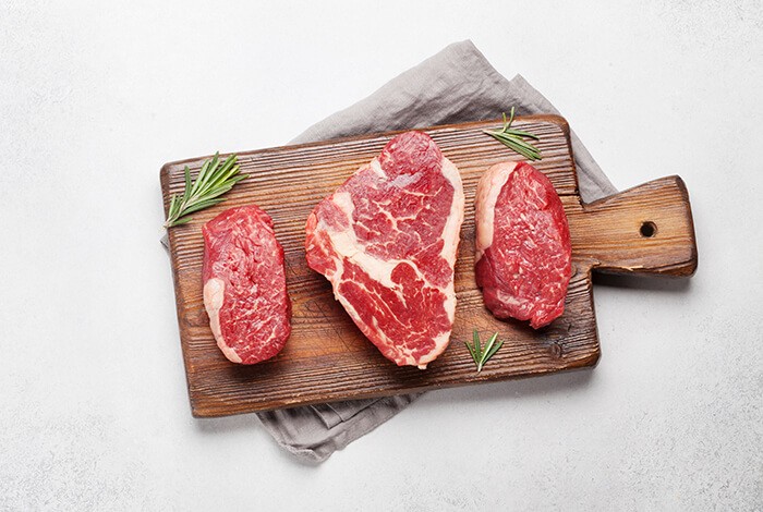 Three slices of beef on a wooden chopping board.