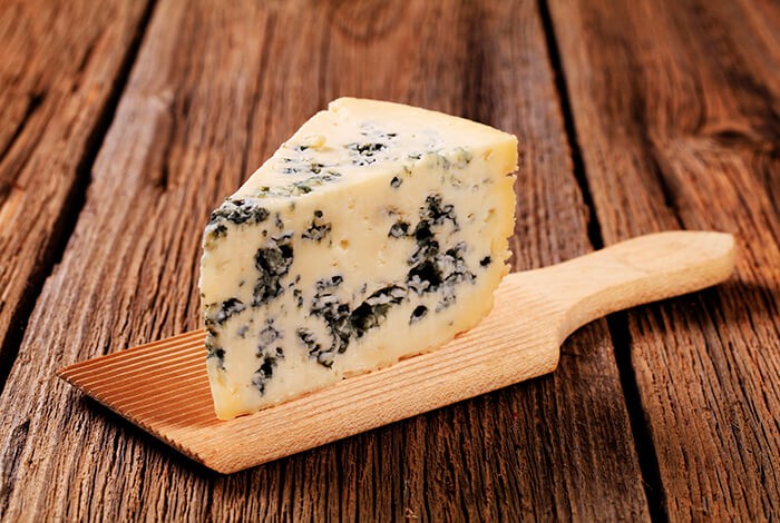 A block of blue cheese on top of a butter paddle.