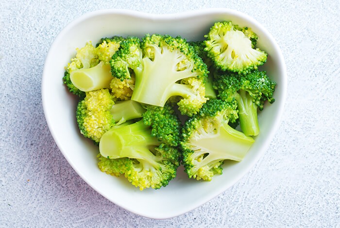 Pieces of cooked broccoli in a heart-shaped bowl.