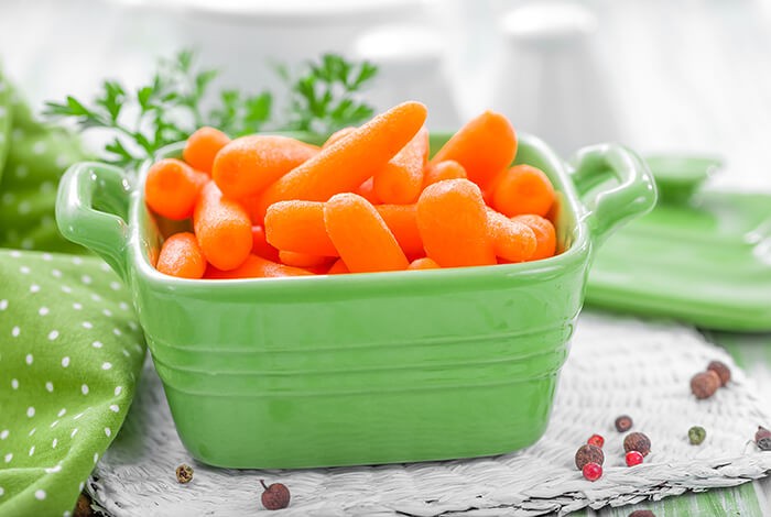 Peeled and cooked baby carrots in a square ceramic bowl.